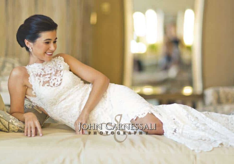 A bride in a lace wedding dress reclining gracefully on a bed.