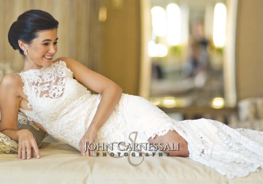 Bride in elegant lace wedding dress reclining on a bed.