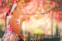 Syracuse Model Photographer Young girl blowing dandelion seeds in a vibrant garden.
