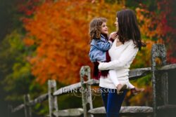 www.JohnCarnessali.com A woman holds a child against a vibrant autumn backdrop.
