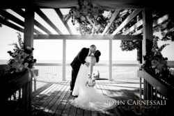 Bride and groom kissing under wooden pergola.