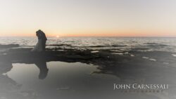 Bride and groom embracing by the water with shoreline in background at Bayshore Grove Oswego NY