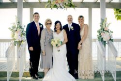 Wedding party smiling under floral arch.
