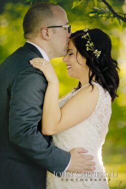 Bride and groom embracing under leafy branches.