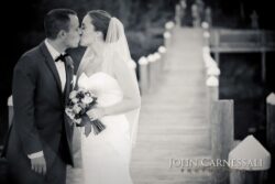 Monochrome newlyweds kissing at end of dock