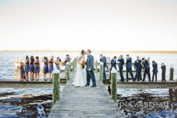 Newlyweds kissing on pier with wedding party