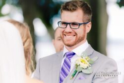 Groom smiling during wedding ceremony outdoors.