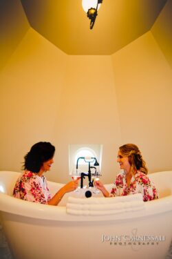 Two women in bathtub, toasting with wine.