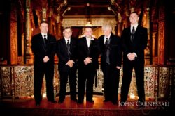 Five men in suits at ornate venue.