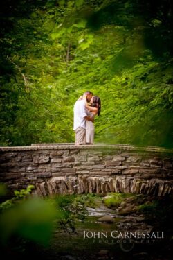 engagement photo of couple kissing on a stone bridge with green forest background,