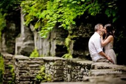 Finger Lakes NY engagement photo of couple kissing by stone wall with gorge greenery, Ithaca area engagement session