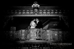 Couple kissing on ornate balcony, black-and-white.