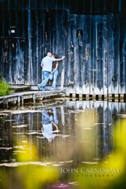 engagement photo of couple reflected in calm water on a wooded walkway,