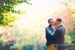 engagement photo of gay couple kissing with bright sun flare and soft pastel background