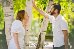 engagement photo of couple playfully raising hands together by birch trees, candid couples portrait