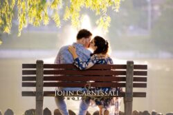 engagement photo of couple kissing on a bench with soft golden light, romantic outdoor portrait