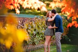 engagement photo of couple kissing near foliage and warm fall color, romantic engagement portrait