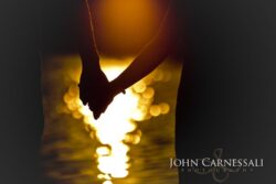 engagement photo of couple holding hands at sunset with glowing reflections, romantic silhouette detail