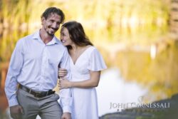 engagement photo of couple standing together near water with bridge in background, romantic outdoor portrait