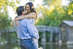 engagement photo of couple hugging with bridge softly blurred in background, romantic natural light portrait