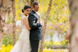 Bride smiling behind groom among yellow leaves
