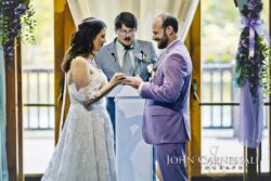 Bride places ring on groom in purple suit