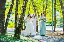 Bride and bridesmaids walking through wooded path.