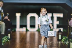 Young boy walking down wedding aisle smiling.