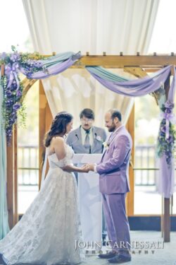 Couple exchanging vows beneath purple floral arch