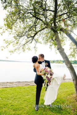 Groom lifting bride by lakeside tree