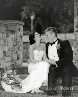 Bride and groom sitting, laughing together outdoors.