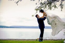 Bride lifted by groom near a lake.