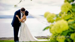 Newlyweds kissing beside lake framed by flowers