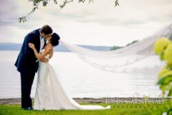 Couple sharing kiss with veil sweeping lake