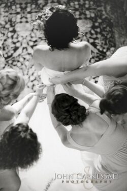 Bride surrounded by bridesmaids adjusting dress.