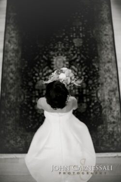 Bride kneeling before ornate tapestry with flowers.