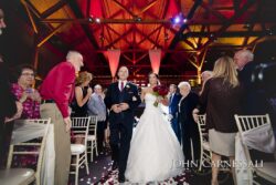 Bride and father walking aisle under timber rafters