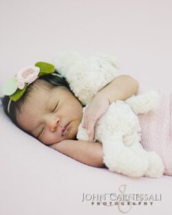 Sleeping newborn baby with a floral headband and stuffed bunny
