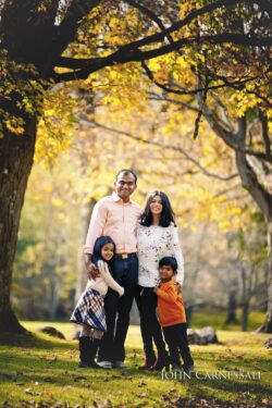 Family of four posing together beneath autumn trees