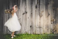 Little girl in a white dress standing by a wooden wall