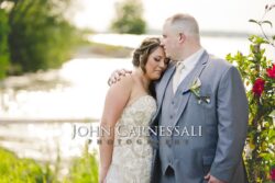 Groom kissing bride's forehead by shoreline
