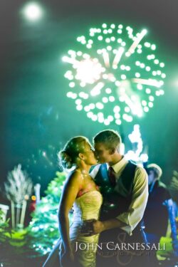 Bride and groom kissing with fireworks in the background.